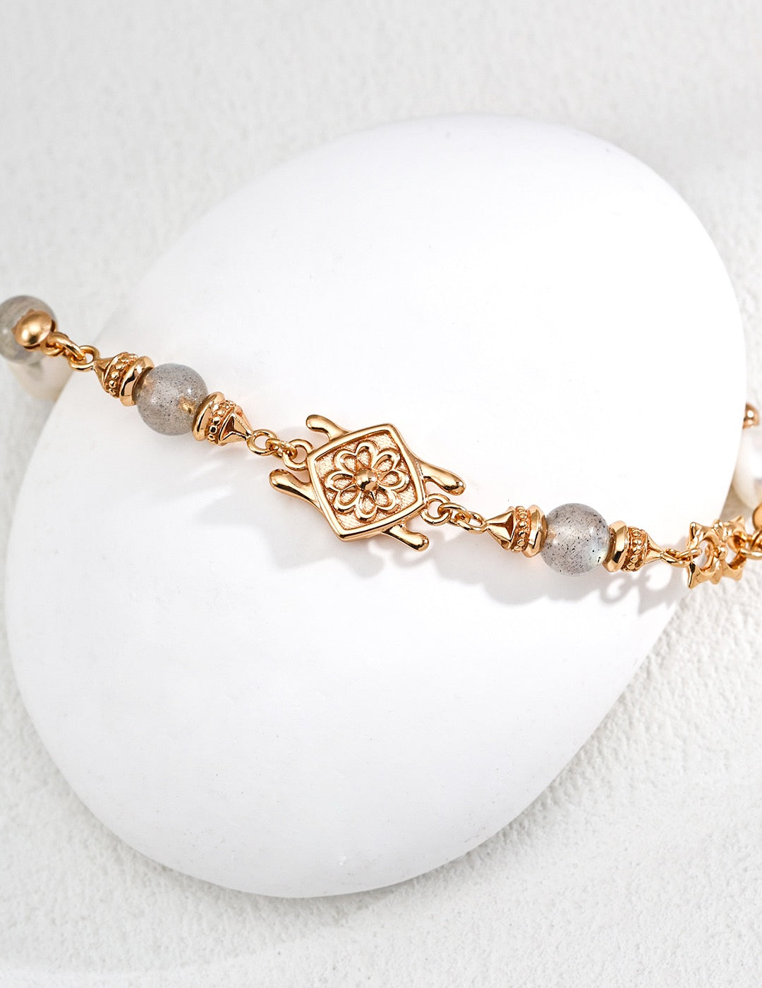 Gold bracelet with Labradorite on a white stone surface