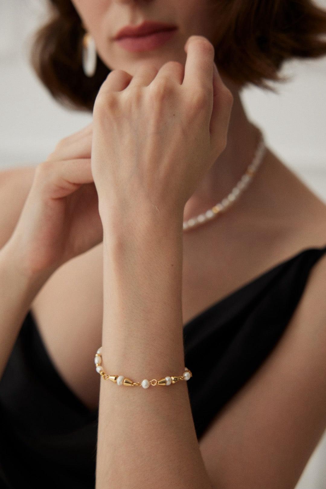 A person wearing a black dress showcasing a gold-plated vine pearl bracelet on their wrist.