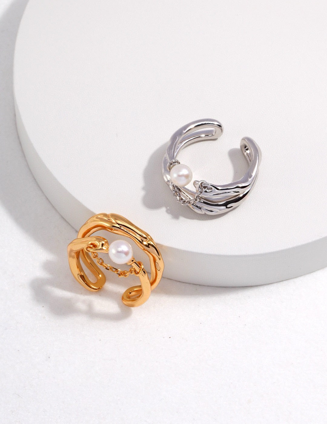 Adjustable gold and silver wave rings with freshwater pearls, styled on a minimalist white surface