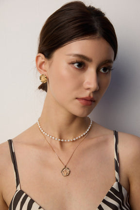 Woman wearing a pearl necklace and earrings against a neutral background