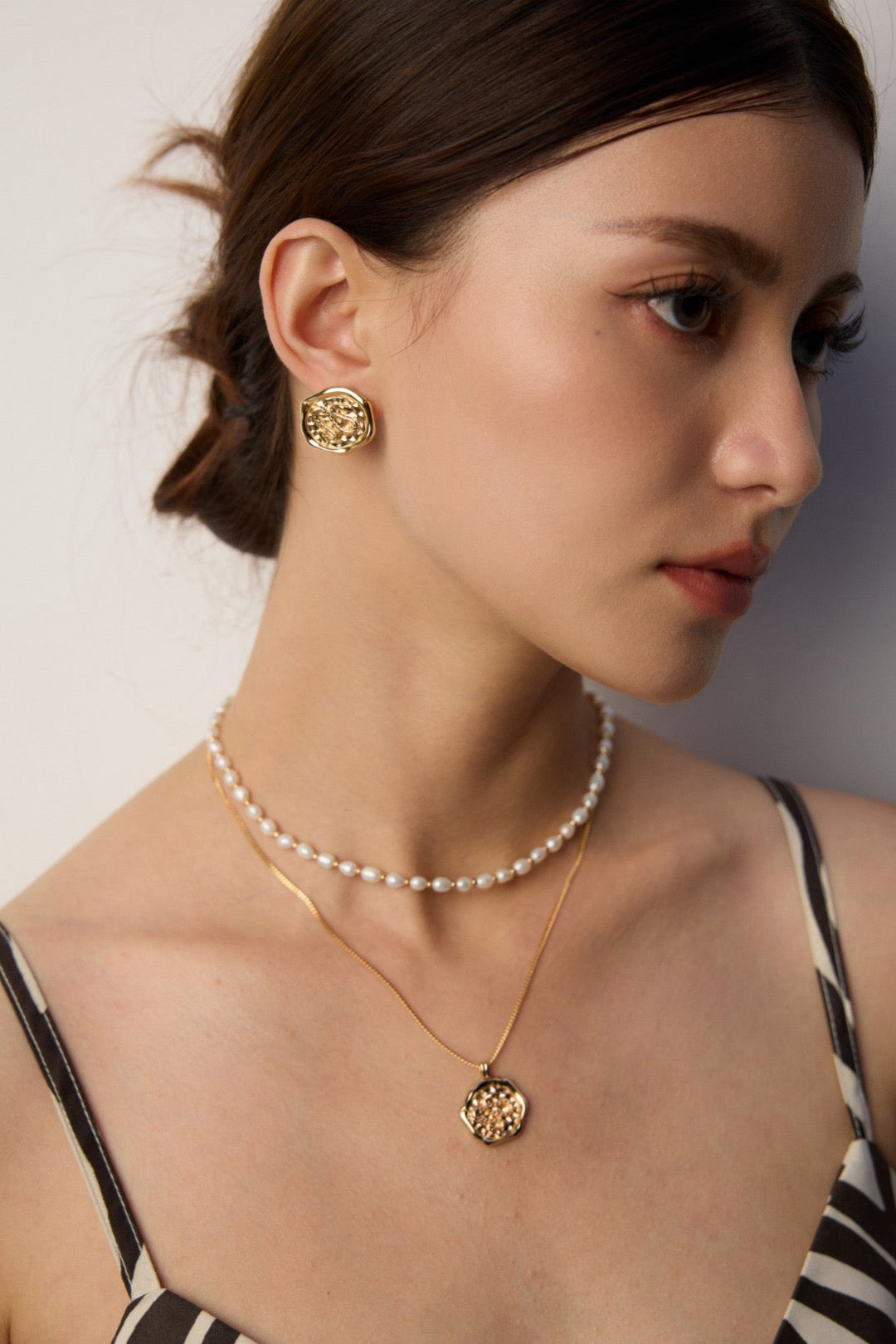 Woman wearing gold earrings and necklace against a neutral background