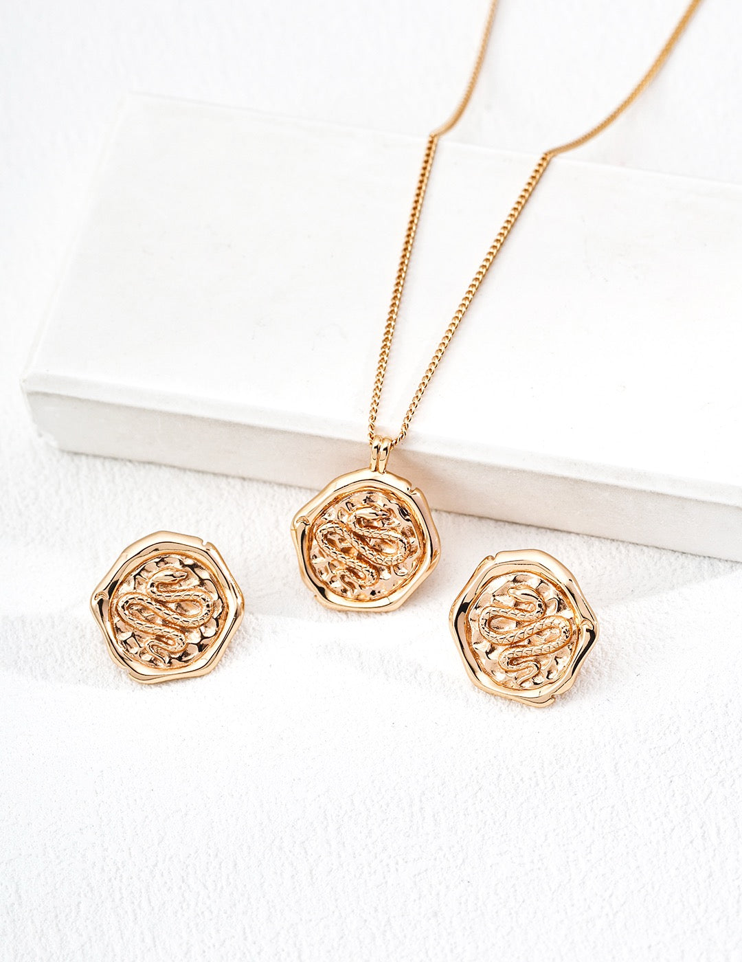 Gold necklace and earrings set on a white surface