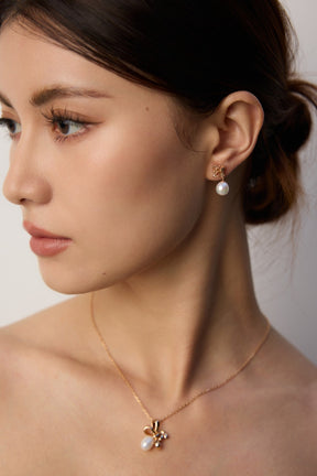 Woman wearing Lia Atelier freshwater pearl flower stud earrings and matching 18K gold vermeil pearl necklace in warm background