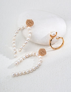 Pearl necklace and earrings with gold evil eye pendants on a white surface