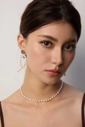 Woman wearing pearl necklace and earrings against a neutral background